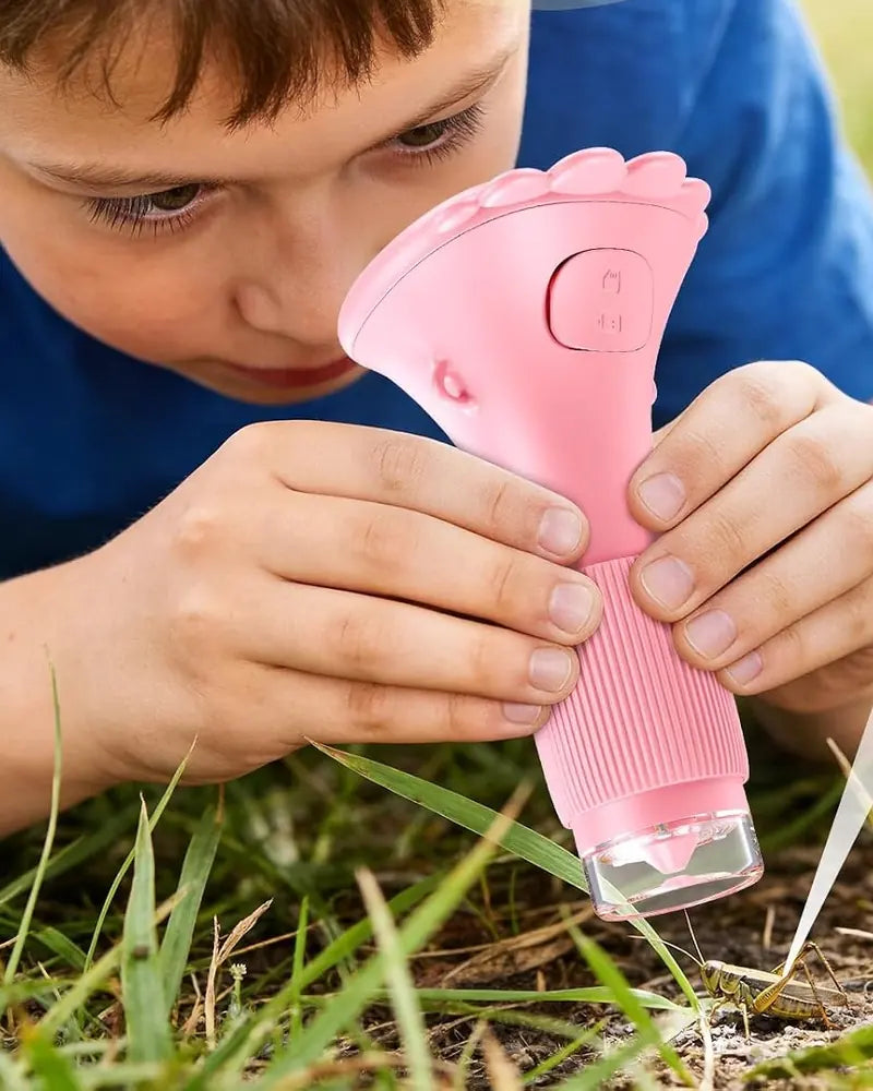 A boy lying in the grass looking through a pink Wondermite Scope